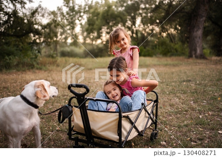 Three little sisters having fun with their dog in a wagon in a park Three little sisters having fun with their dog in a wagon in a park 130408271