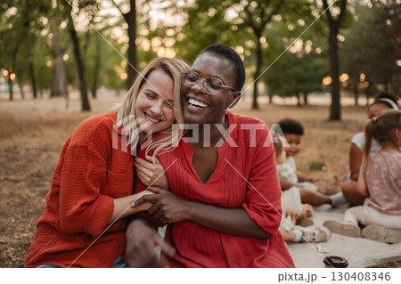 Two Smiling Women Embracing at a Park Picnic 130408346