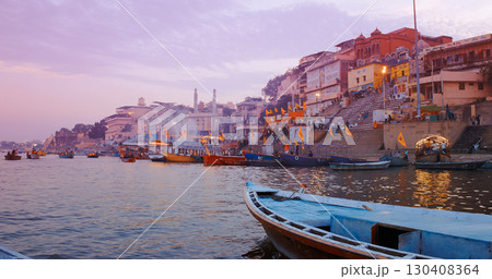 Varanasi, Uttar Pradesh, India. Cityscape Skyline In Evening Lights. Evening Pink Purple Sunset Sky, Dusk . Camera Moving Along Riverbank Embankment. Cinematic View From Boat Ride Past Darbhanga Ghat 130408364