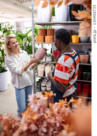 Shop assistant showing flowerpots to customer in garden center 130408735