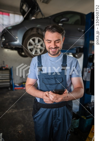 Happy mechanic using mobile phone in a car repair shop 130408752