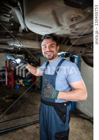 Smiling mechanic inspecting car chassis and showing thumbs up Smiling mechanic inspecting car chassis and showing thumbs up 130408753