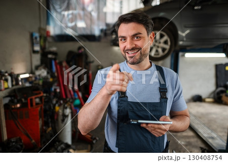 Mechanic pointing with finger and holding tablet in auto repair shop Mechanic pointing with finger and holding tablet in auto repair shop 130408754