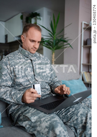 Soldier making online payment using laptop and credit card at home Soldier making online payment using laptop and credit card at home 130408774