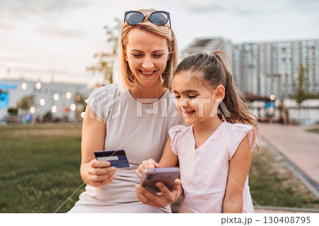 Mother and daughter making online payment using credit card and smartphone in city park Mother and daughter making online payment using credit card and smartphone in city park 130408795