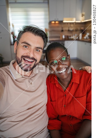 Young multi-ethnic couple taking a selfie while sitting on the sofa at home Young multi-ethnic couple taking a selfie while sitting on the sofa at home 130408827