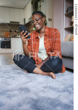 Young woman using smartphone at home sitting on carpet Young woman using smartphone at home sitting on carpet 130408851