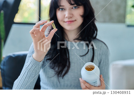 Close up of yellow Omega 3, fish oil capsule and bottle in hands of young woman 130408931