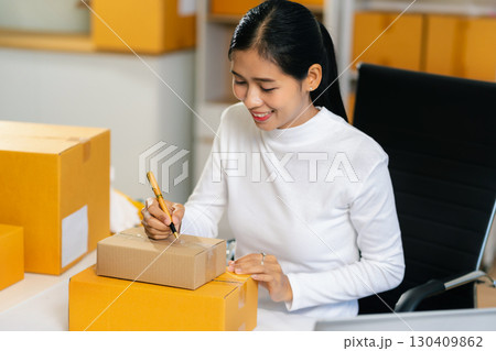 Woman start up small business owner writing address on cardboard box at workplace.small business entrepreneur SME or freelance asian woman working with box at home. 130409862