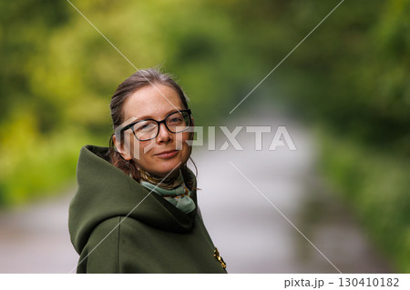 Woman enjoying a peaceful moment outdoors in a park on a sunny day surrounded by greenery 130410182