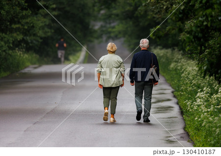 Couple walks leisurely along a serene, tree-lined road on a cloudy day Couple walks leisurely along a serene, tree-lined road on a cloudy day 130410187