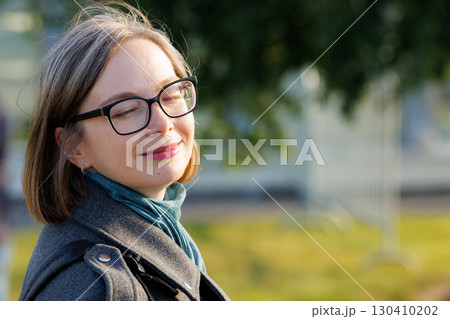 Woman enjoying a sunny day outdoors with eyes closed and a peaceful expression 130410202