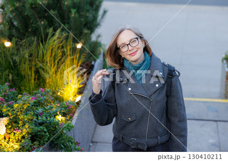 Woman in stylish coat stands by plants and smiles in urban setting during daylight 130410211