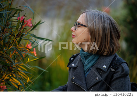 Woman admiring flowers in a garden during daylight hours in a lush natural setting Woman admiring flowers in a garden during daylight hours in a lush natural setting 130410225