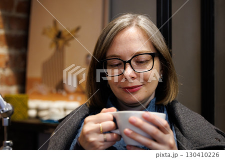 Woman enjoying a warm drink in a cozy cafe during a calm afternoon with brick wall decor 130410226