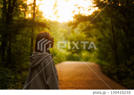 Woman enjoys a peaceful moment on a forest path during sunset surrounded by vibrant greenery Woman enjoys a peaceful moment on a forest path during sunset surrounded by vibrant greenery 130410238