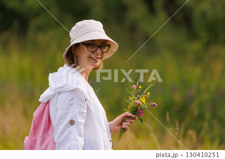 Smiling young woman holding wildflowers in a green meadow during a sunny day in summer 130410251