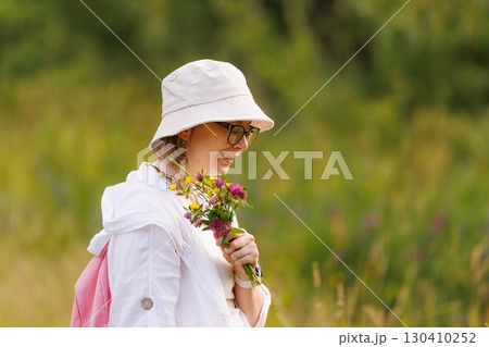 Young woman with glasses collects wildflowers in a sunny field during a warm afternoon Young woman with glasses collects wildflowers in a sunny field during a warm afternoon 130410252