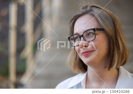 Woman with glasses smiles outdoors, showcasing a relaxed expression in a natural setting 130410266