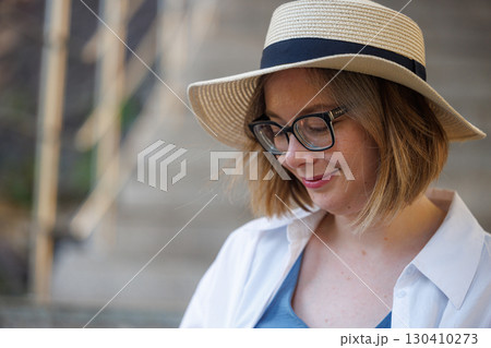 Woman in a straw hat enjoying a quiet moment outdoors near stairs on a sunny day Woman in a straw hat enjoying a quiet moment outdoors near stairs on a sunny day 130410273