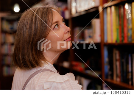 Woman exploring bookshelves in a cozy library setting during a quiet afternoon 130410313