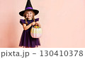 Child dressed as a witch holding a pastel pumpkin bucket for candy 130410378