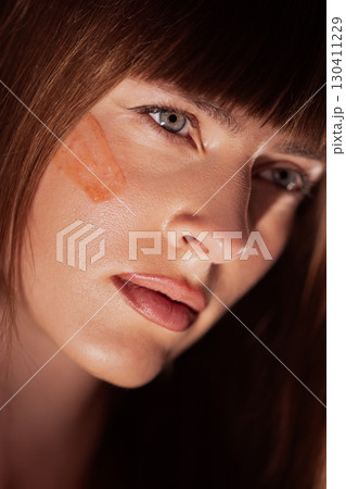 Woman with clay mask stripe on cheek showing natural skincare ritual Woman with clay mask stripe on cheek showing natural skincare ritual 130411229