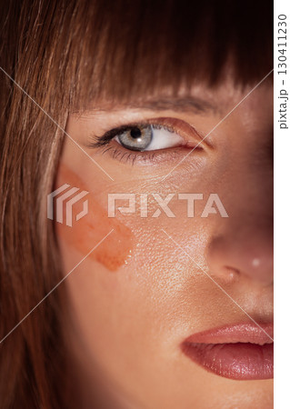 Woman face closeup with red clay mask applied under eye for skincare Woman face closeup with red clay mask applied under eye for skincare 130411230