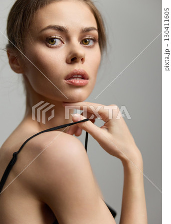 Elegant young woman with natural makeup posing gracefully, showcasing a delicate expression, against a soft, neutral background. Fashion and beauty concept. 130411605