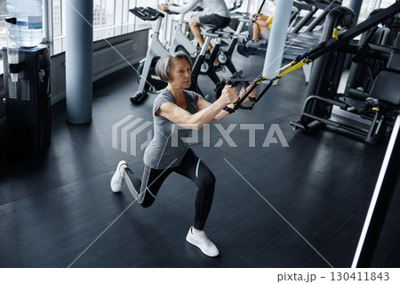 An older woman is exercising on a suspension trainer at a gym An older woman is exercising on a suspension trainer at a gym 130411843