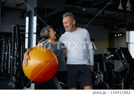 A man and a woman in a gym with an orange exercise ball 130411862