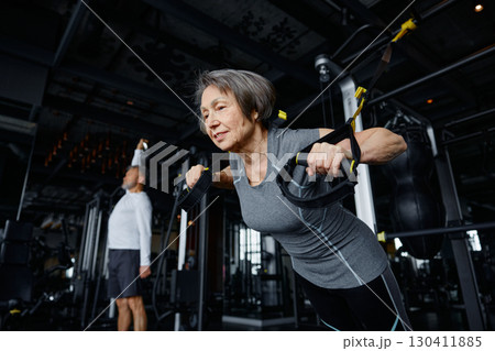 An older woman is performing push ups on a specialized machine in a gym An older woman is performing push ups on a specialized machine in a gym 130411885