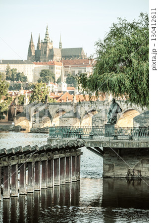 A statue of composer Bedrich Smetana stands near the river, overlooking the stunning panorama of Prague, with its iconic castle and historic architecture in the background. 130412611