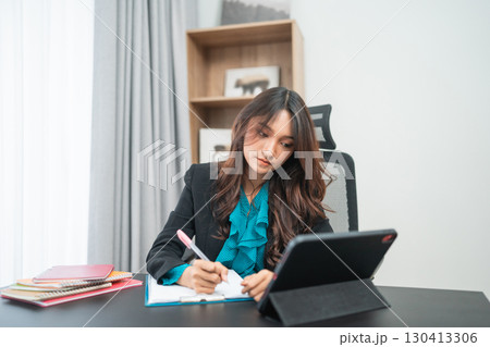A Professional Woman Engaged in Work at Her Desk Using a Tablet and a Notepad 130413306