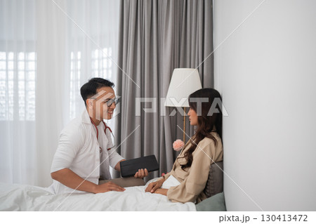 A Doctor is Consulting with a Patient in a Comfortable, Cozy Bedroom Environment 130413472