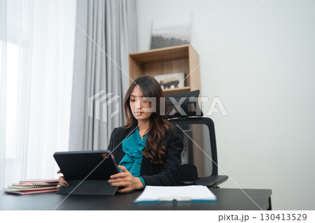 Professional Woman Working at Desk with Tablet in Modern Office Environment 130413529