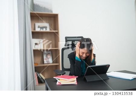 A stressed businesswoman is working in her home office with a device nearby 130413538