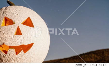 Unusual white Halloween pumpkin with carved smiling face on countryside field with clear evening sky background 130414117