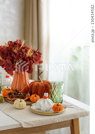 Thanksgiving table setting with decorative pumpkins, candles and string lights on white wooden table 130414582