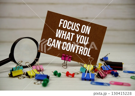 Focus On What You Can Control text on paper card with magnifying glass and stationary on wooden background 130415228