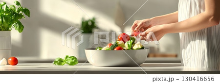 Woman preparing a healthy meal, adding fresh cherry tomatoes to a bowl of steaming broccoli, cauliflower, and other vegetables, in a sunlit kitchen, promoting healthy eating and home cooking 130416656