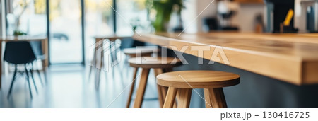 Empty wooden stools stand next to a long, light wooden counter in a modern kitchen, creating a warm and inviting atmosphere with natural materials 130416725