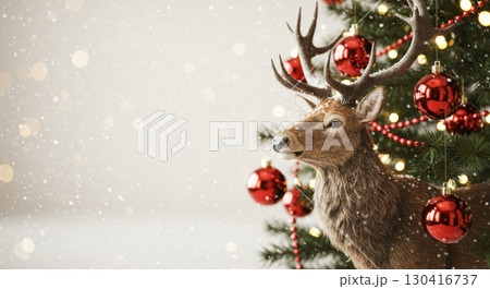 Christmas deer next to a decorated fir tree with red ornaments and falling snow on a white background.  130416737