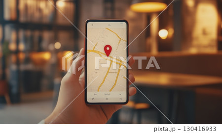 Businessman holding a smartphone with a navigation app displaying a red pin on an online map, indicating a specific location in a restaurant or nearby area 130416933