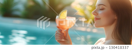 Young woman holding a refreshing cocktail by the poolside, enjoying the summer sun and tropical ambiance during her vacation at a luxurious resort 130418337