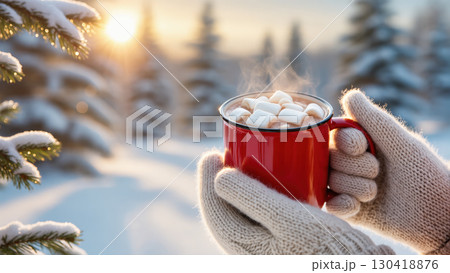 Christmas hot chocolate with marshmallows in red mug held by cozy mittens in snowy forest at sunset 130418876