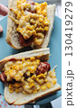 Two hot dogs topped with creamy corn and melted cheese on a blue plate 130419279