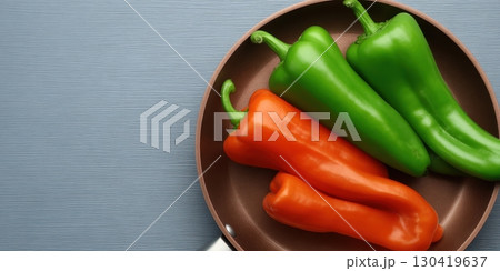 Three bell peppers, one orange and two green, rest in a copper frying pan on a gray surface Three bell peppers, one orange and two green, rest in a copper frying pan on a gray surface 130419637