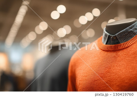 An orange sweater is showcased on a mannequin in a contemporary store. Soft, blurred lights create a warm ambiance, enhancing the focus on the apparel. An orange sweater is showcased on a mannequin in a contemporary store. Soft, blurred lights create a warm ambiance, enhancing the focus on the apparel. 130419760