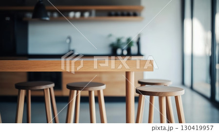 Natural light illuminates a contemporary kitchen featuring a sleek wooden table and matching stools, creating a warm and inviting atmosphere perfect for modern living 130419957